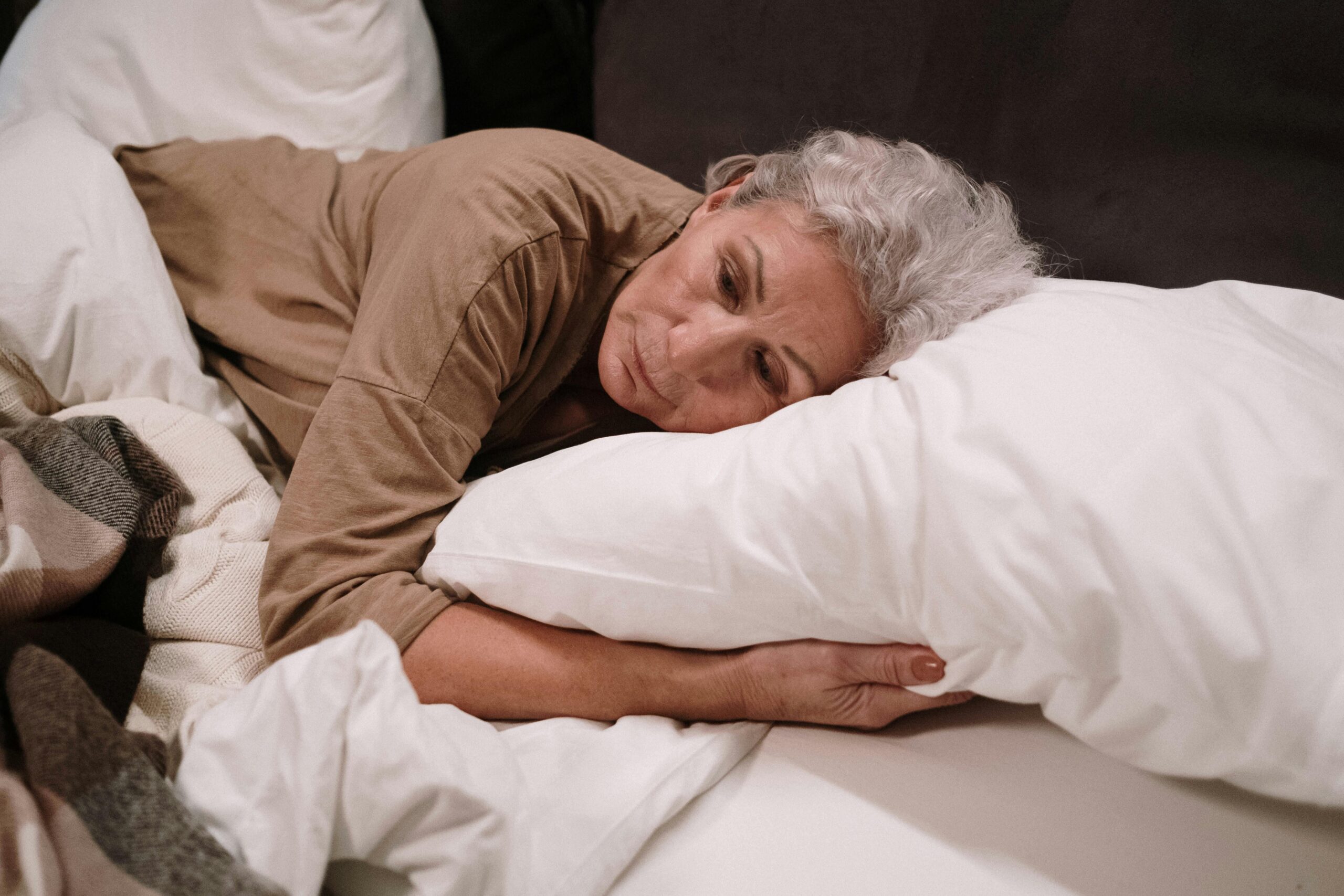 ältere Frau liegt im Bett und umgreift ihr Kopfkissen