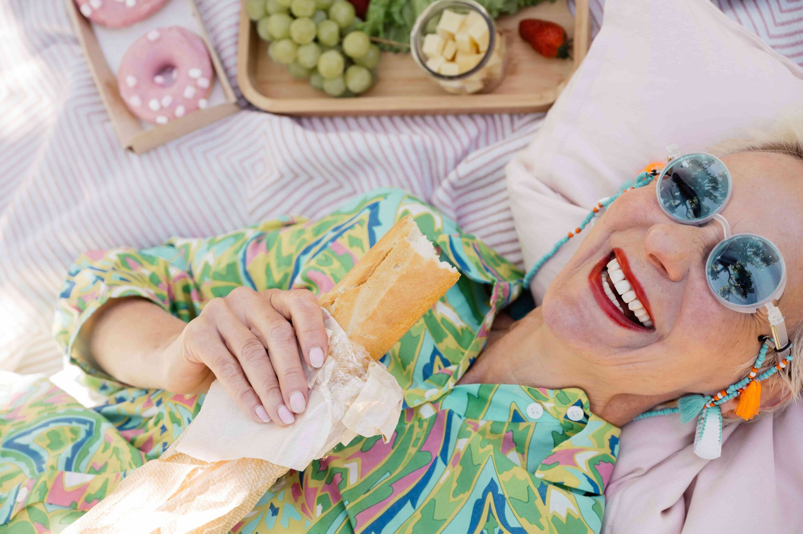 eine ältere Frau hält glücklich lachend ein Baguette in der Hand beim Picknick - Lebensfreude