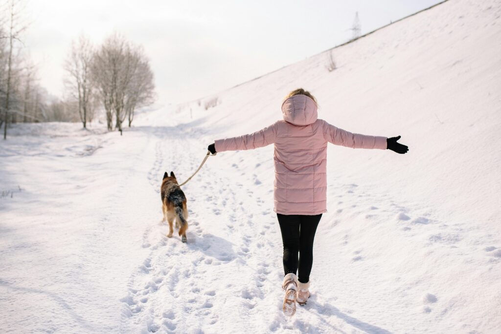Frau geht mit ihrem Hand im Schnee spazieren