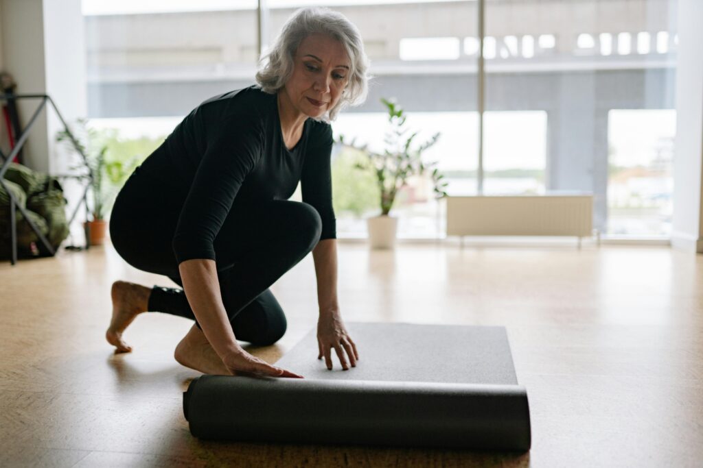 Frau rollt zuhause ihre Yogamatte aus - Fitness ab 50