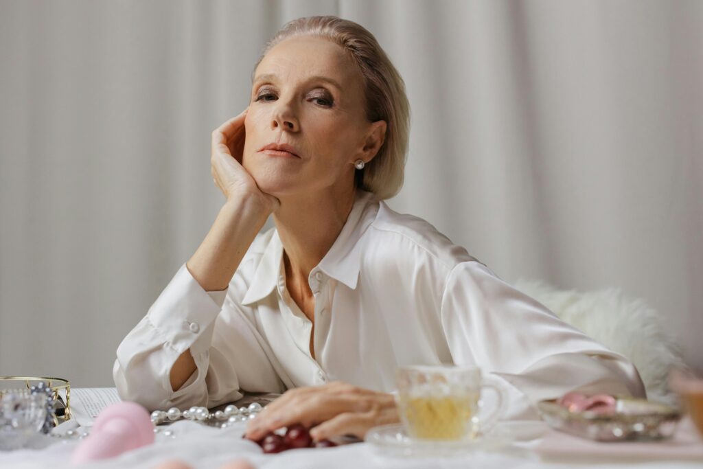 Portrait einer älteren attraktiven Frau. Sie stütz ihren Kopf auf ihre Hand und blickt etwas von oben herab in die Kamera. Beauty & Anti-Aging