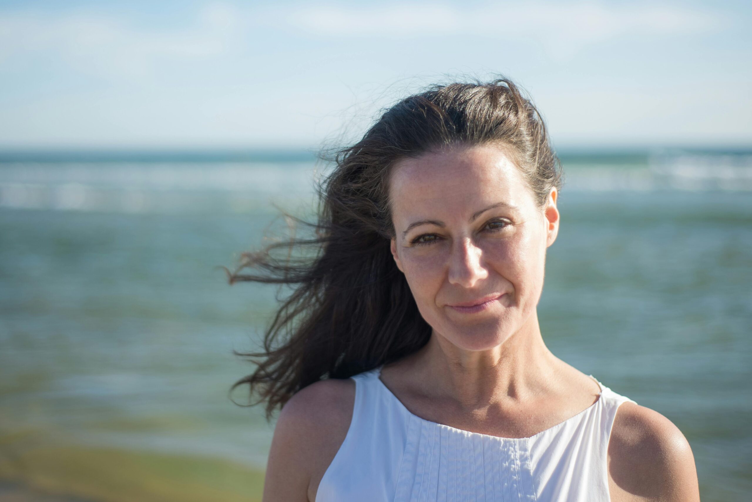 Portrait einer attraktiven älteren Frau. Sie lächelt in die Kamera, das Meer im Hintergrund. Natürlich jünger aussehen ab 50