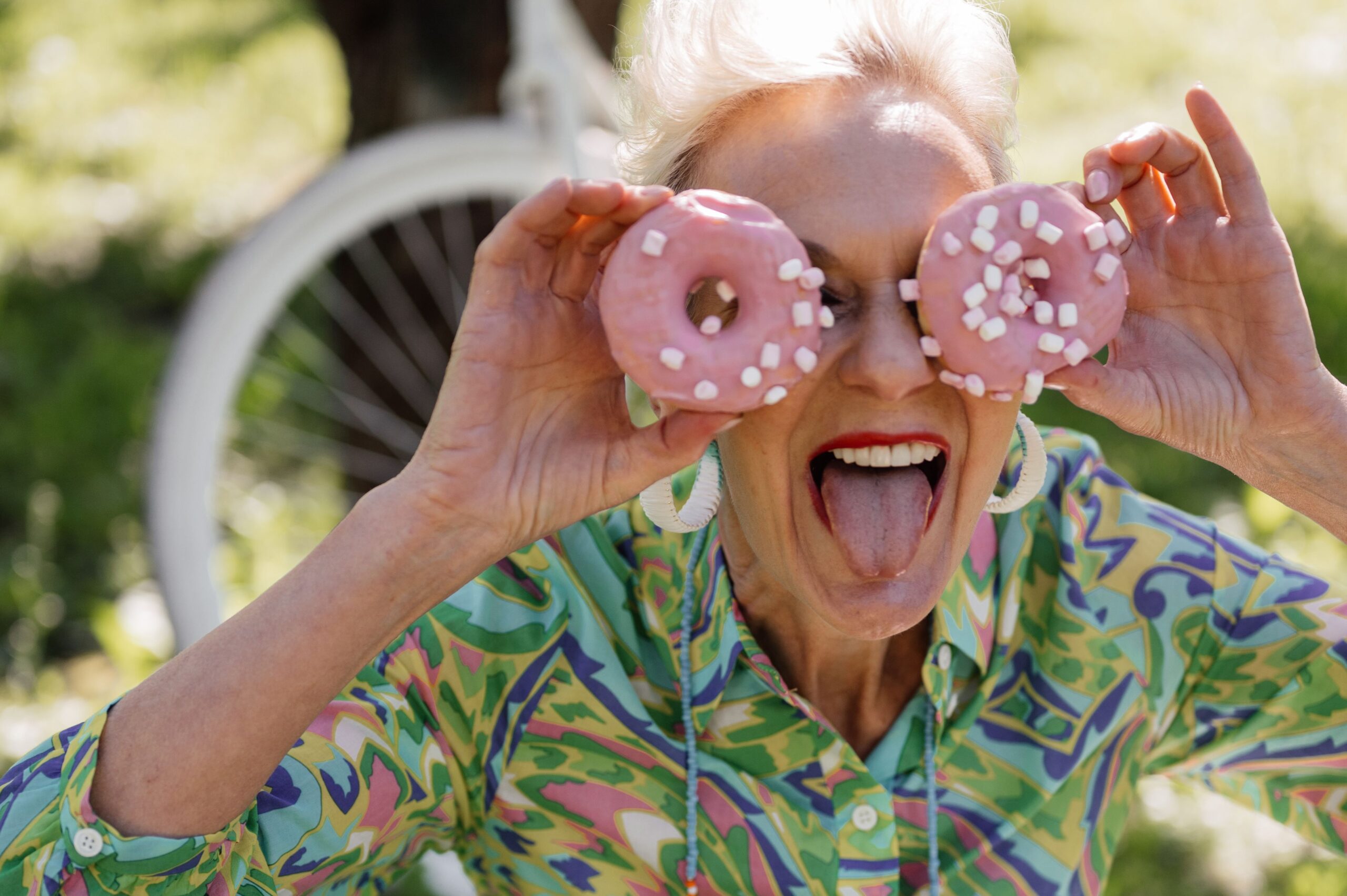 ältere Frau blickt durch Donat-Ringe hindurch - Zucker und Longevity