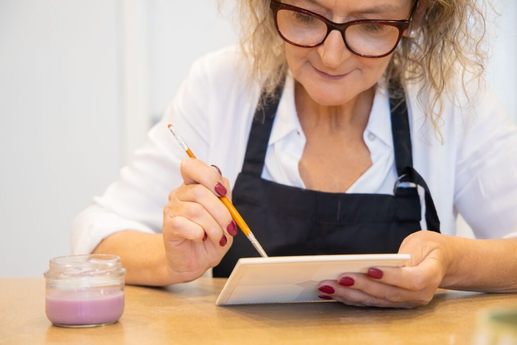 ältere Frau bemalt eine Kachel